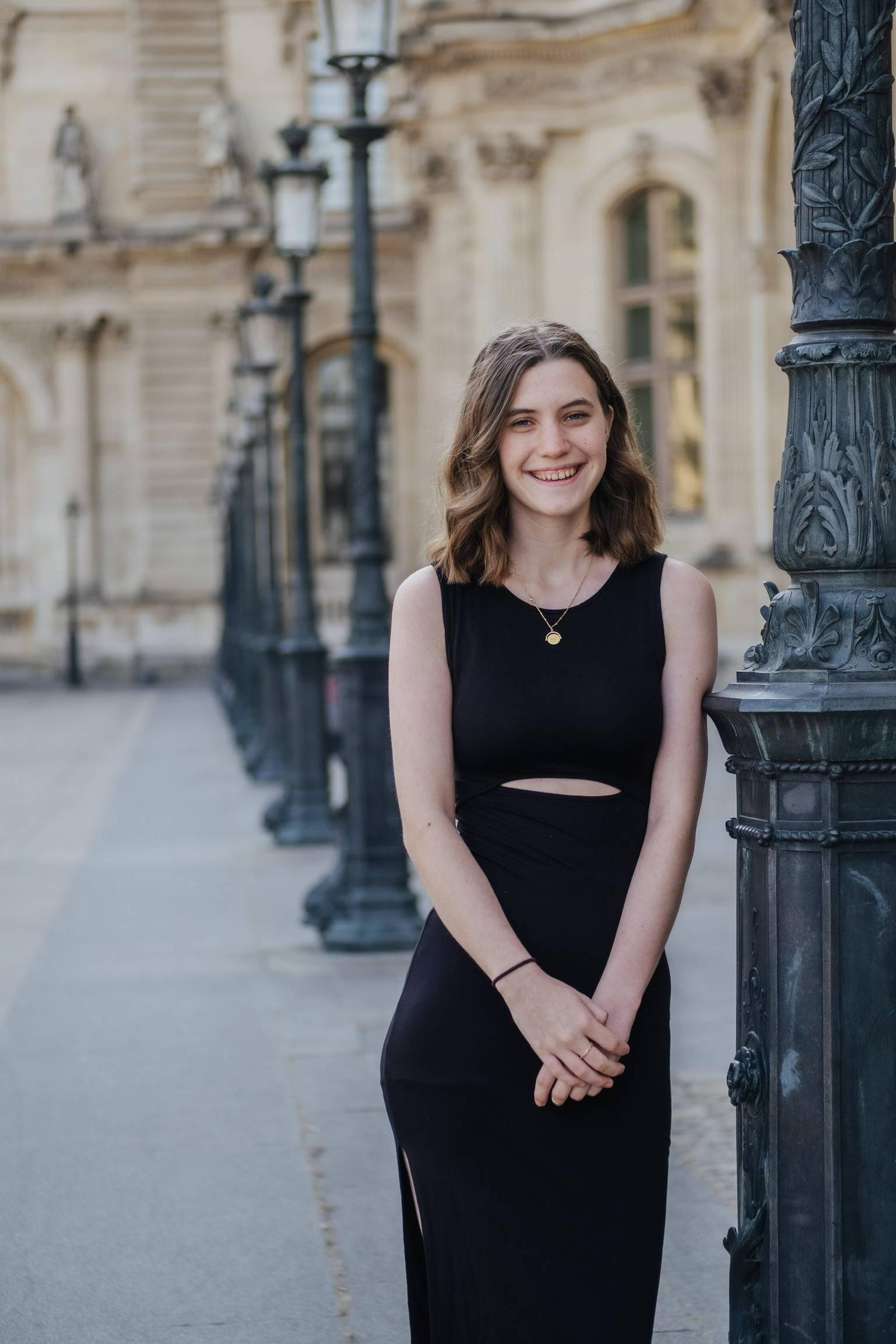 Girl in black dress smiling next to light pole